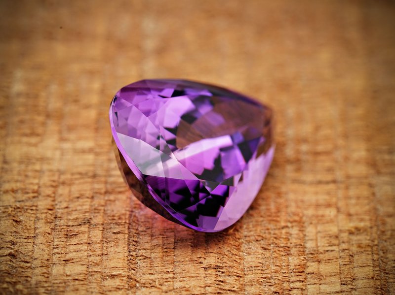 Close-up image of a sparkling purple amethyst gemstone on a textured surface.