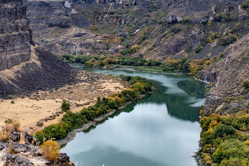 A stunning view of a tranquil river winding through a rocky canyon in autumn, showcasing vibrant foliage.