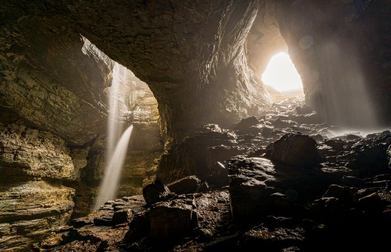 Dramatic cave view with backlit entrance and cascading waterfalls creating a mystical atmosphere.