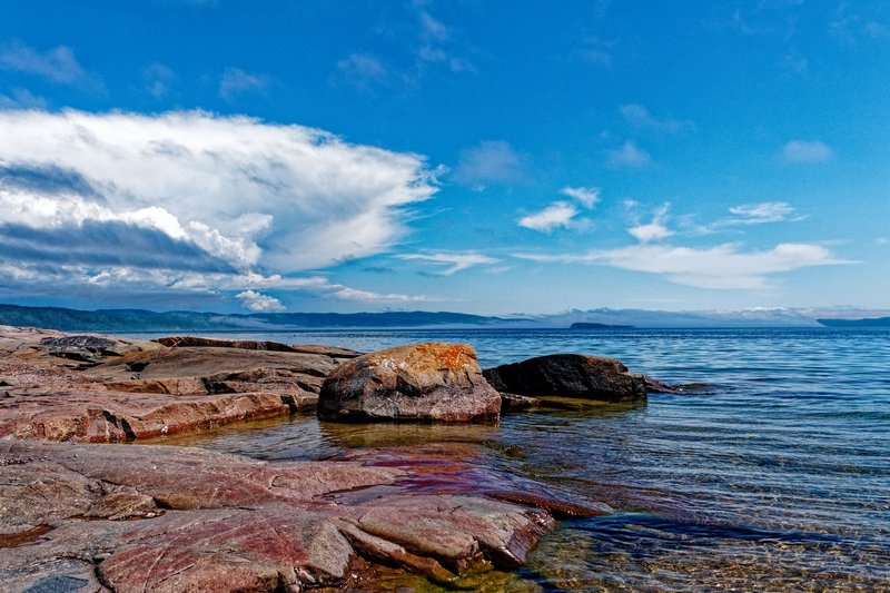 Tranquil view of Lake Superior's rocky shoreline in Thunder Bay, under a vibrant blue sky.