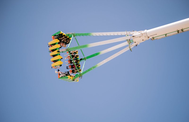People enjoying a thrilling amusement park ride suspended midair against a clear blue sky.