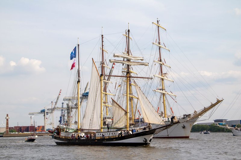 Majestic tall ships with large sails in Hamburg's port on the Elbe River.
