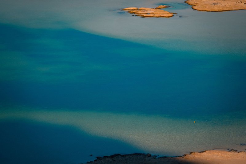 A serene aerial shot capturing the tranquil turquoise waters of a lake under the sunlight.
