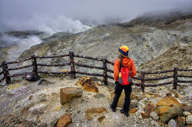 Hiker in vibrant attire gazing at misty volcanic landscape in Jawa Barat, Indonesia.