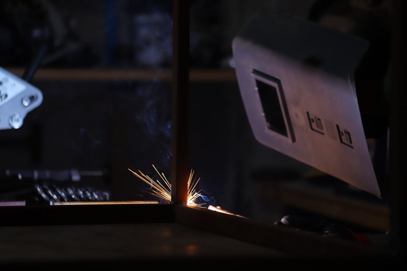 Close-up of a welding process in a dark workshop showing bright sparks and protective gear.