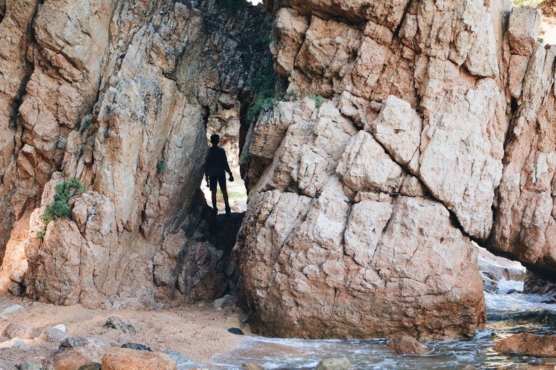 Silhouette of a person exploring a rocky coastal cave formation, capturing adventure in nature.