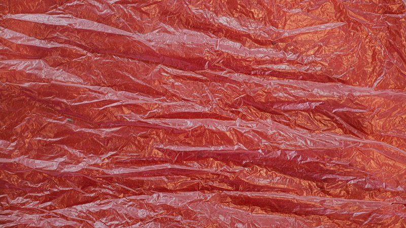 Closeup of crumpled red plastic sheet with a glossy and translucent texture.