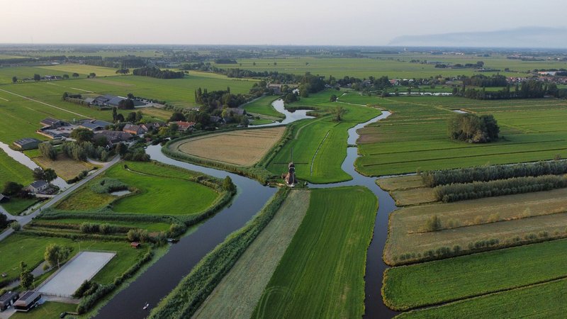 Aerial drone shot of picturesque Dutch countryside with fields, rivers, and a windmill.