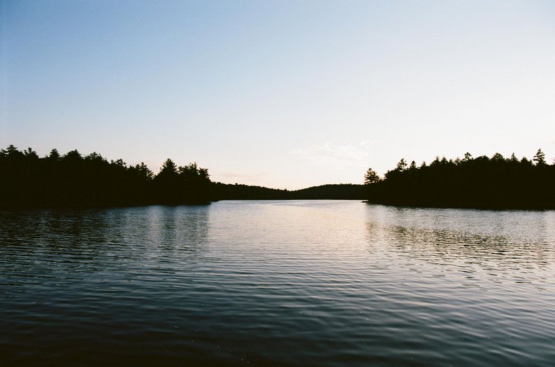 Peaceful lake with surrounding forest in Algonquin Park, Ontario, captured during a tranquil sunset.