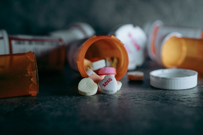 Close-up of open medicine bottles with colorful pills scattered on a dark surface.