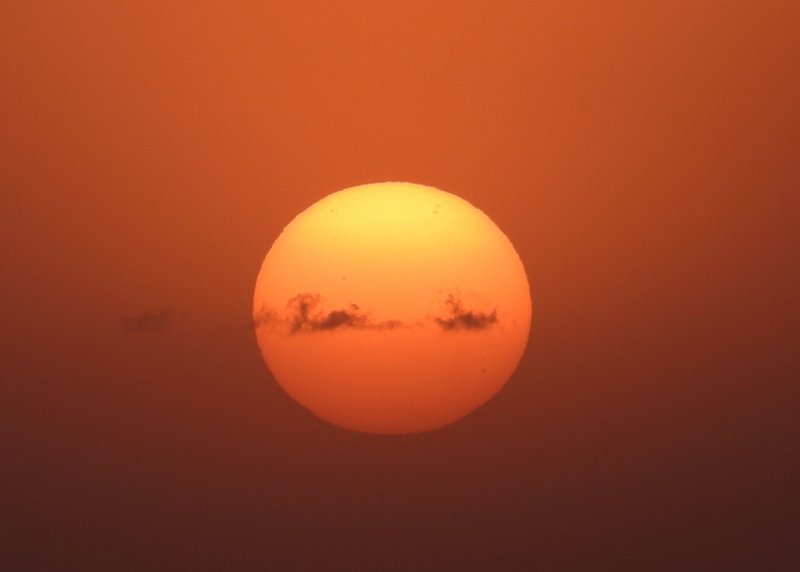 A breathtaking close-up of the sun with dramatic clouds in a warm orange sky.