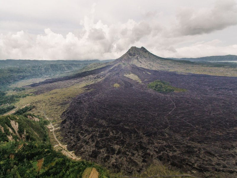 A breathtaking aerial view of a volcanic mountain with sprawling lava fields under cloudy skies.