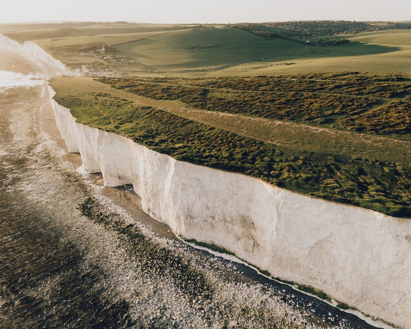 Stunning aerial photograph capturing the iconic white cliffs, lush fields, and serene seaside in natural beauty.