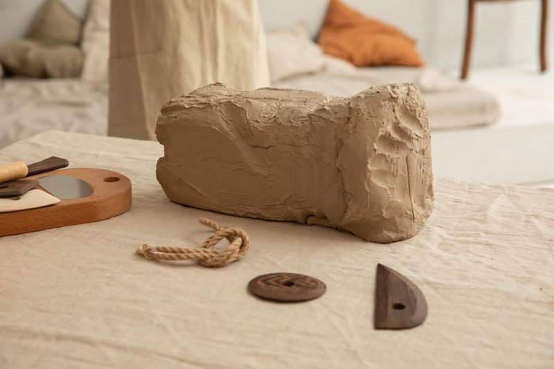 Blurred crop master in apron standing near table with pottery tools and big piece of clay in light craft workshop