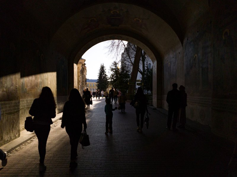 Silhouetted figures walk through a historic archway in Sergiyev Posad, Russia on a sunny day.