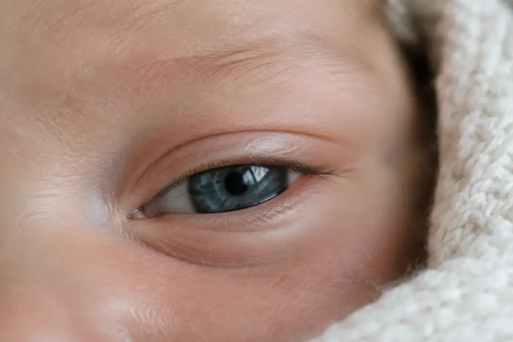 A newborn baby's slate gray-blue eye, half open, beside a cream knit blanket