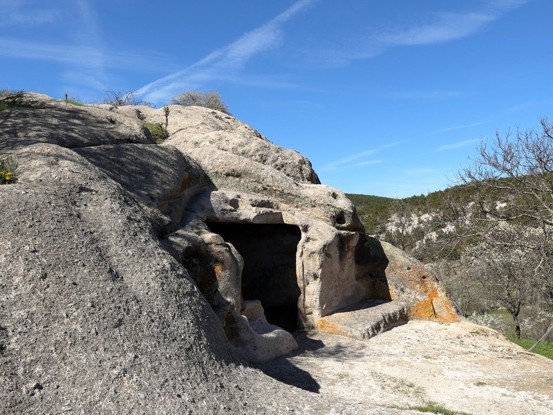 Explore an ancient rock cave set against a clear blue sky in a rugged landscape.