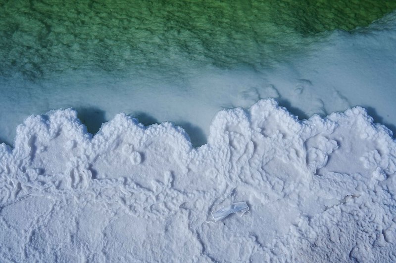 Aerial view of white salt formations contrasting with green water at a salt lake.