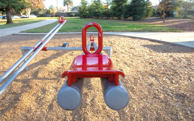 Close-up of a red seesaw in an outdoor sunny playground setting.