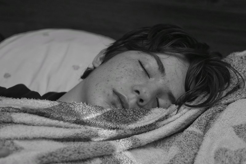 Black and white photo of a teenage boy sleeping peacefully wrapped in a blanket.