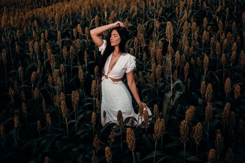 A woman in a white dress posing amidst a lush sorghum field in Brazil, exuding serenity.
