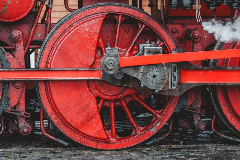 Detailed view of an old steam locomotive's red wheel and pistons, showcasing industrial engineering.