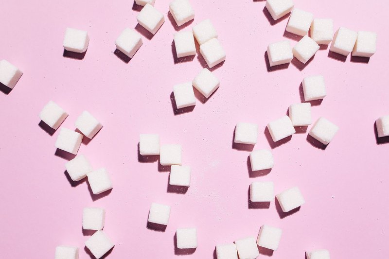 Flat lay of sugar cubes scattered over a pink surface, modern and bright.