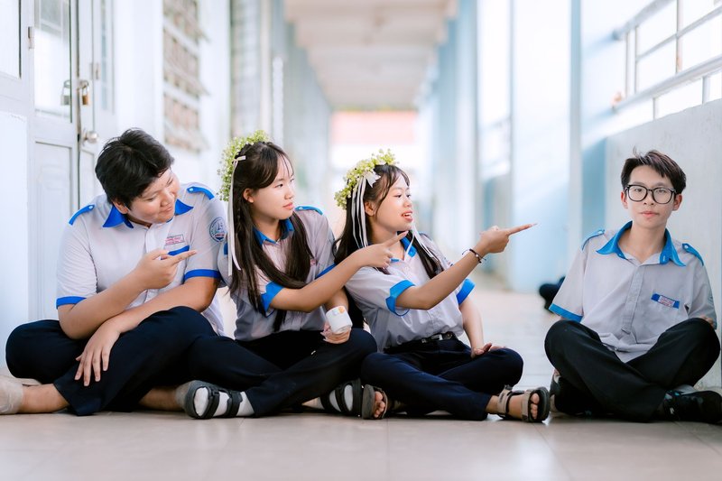 Group of teenagers in school uniforms sitting and interacting in hallway.
